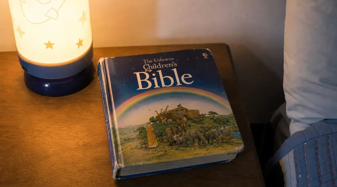 The Beginner's Bible on a nightstand next to a small lamp, showing light wear from regular use